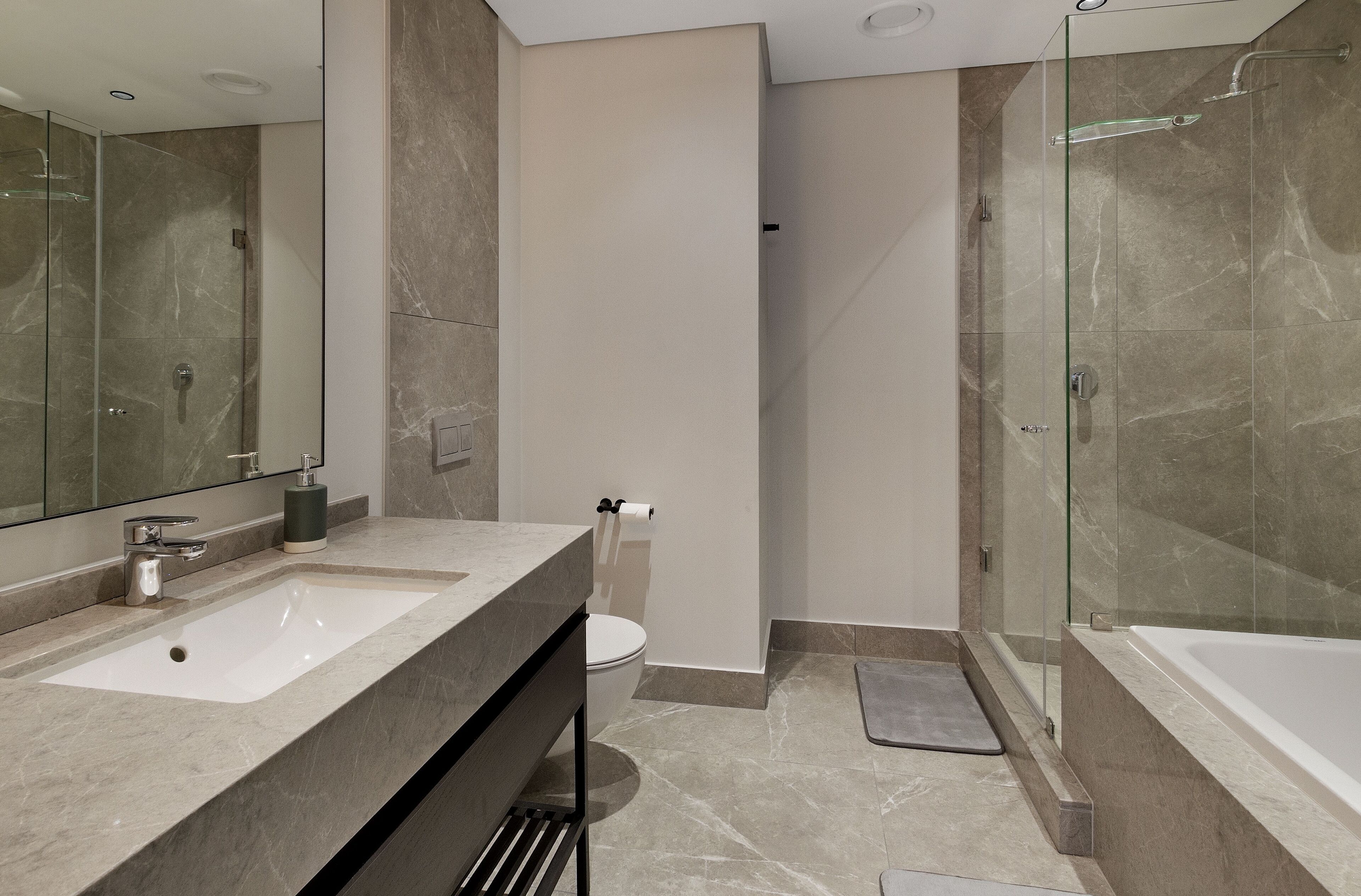 A modern bathroom with a large mirror, a sink, a toilet, and a glass-enclosed shower area.