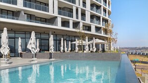 A modern hotel with a pool, outdoor umbrellas, and a view of the city. - Ellipse Waterfall 31015 (Midrand)