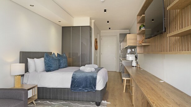 A modern bedroom with a bed, bedside tables, a TV mounted on the wall, and a wooden desk. - Ellipse Waterfall 31015 (Midrand)