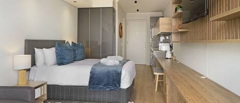 Une chambre à coucher moderne, avec un lit, des tables de chevet, un téléviseur fixé au mur et un bureau en bois.