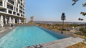 Una piscina con sillones de descanso y sombrillas, rodeada por un edificio moderno con balcones.