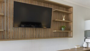 Una cocina moderna con televisor empotrado, paneles de madera y una encimera con hervidor y tazas.