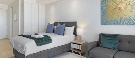 A modern bedroom with a bed, nightstand, and sofa.
