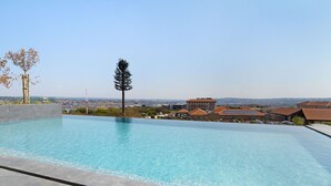 A rectangular swimming pool with clear blue water, surrounded by a tiled deck. In the background, there are residential buildings with brown roofs and a clear sky.