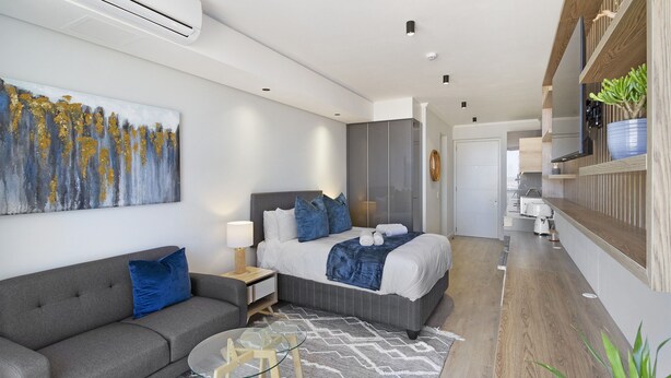 A modern hotel room with a bed, a sofa, a glass table, and a painting on the wall.