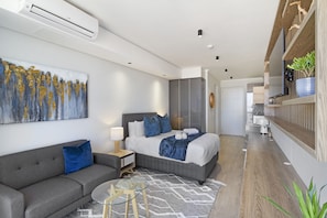 A modern hotel room with a bed, a sofa, a glass table, and a painting on the wall.