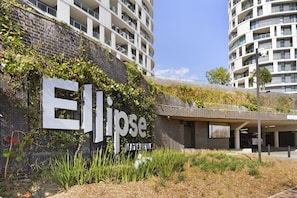 Een modern gebouw met een opvallend 'Ellipse'-bord, omgeven door groen en een parkeerplaats.