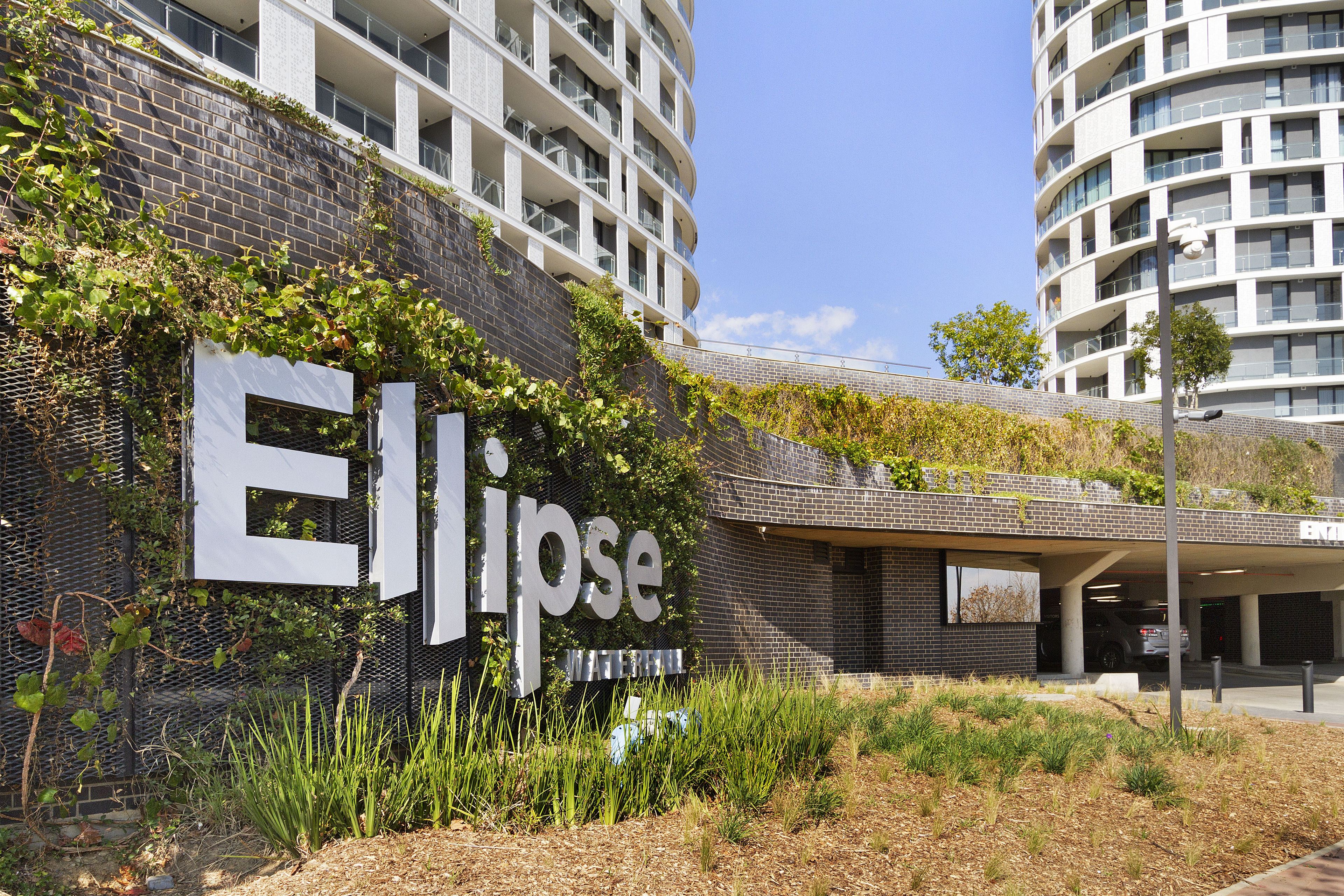 Un edificio moderno con un llamativo letrero 'Ellipse', rodeado de vegetación y un área de estacionamiento.
