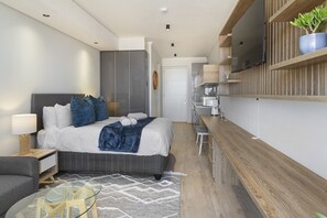 A modern hotel room with a bed, bedside table, lamp, and a TV mounted on the wall.