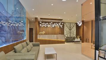 En moderne lobby med reception, sofa, sofabord og en dekorativ væg med hængende lamper.