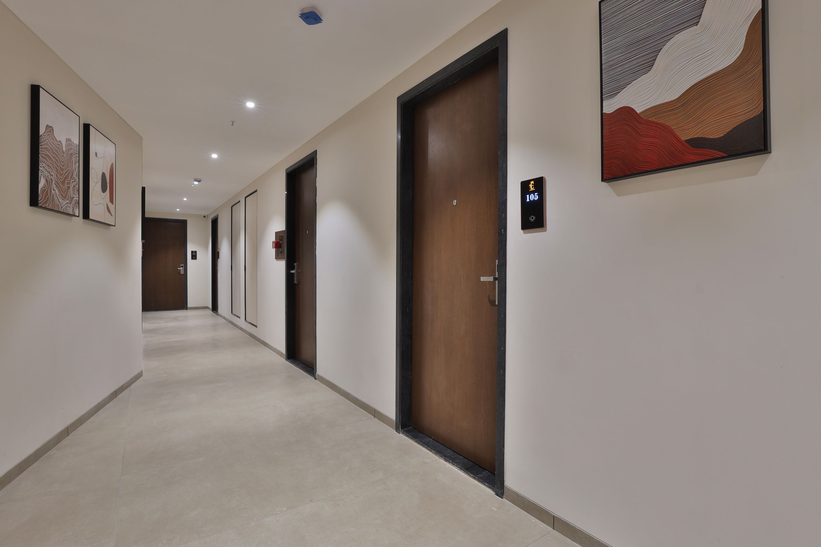 A hotel hallway with doors, numbered room signs, and framed artwork on the walls.