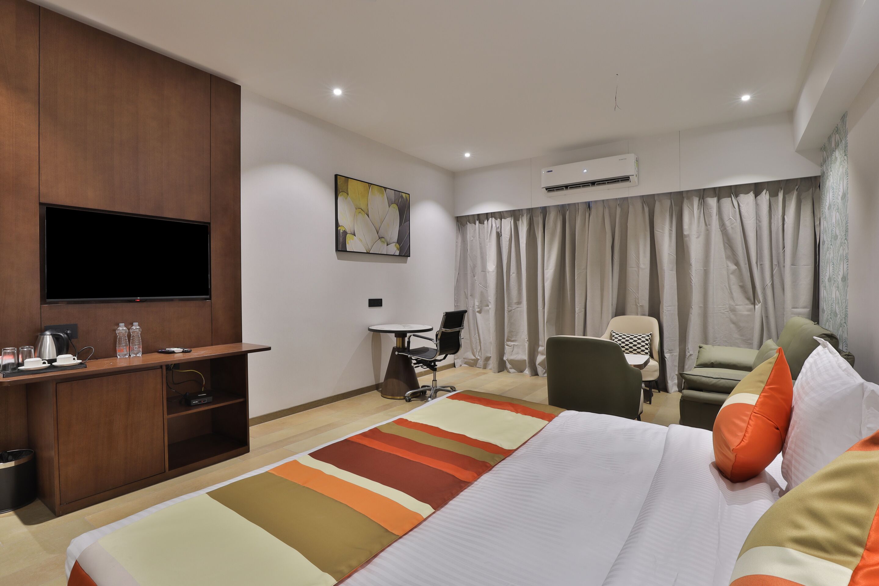 A hotel room with a bed, a desk, a chair, a television, and an air conditioning unit.