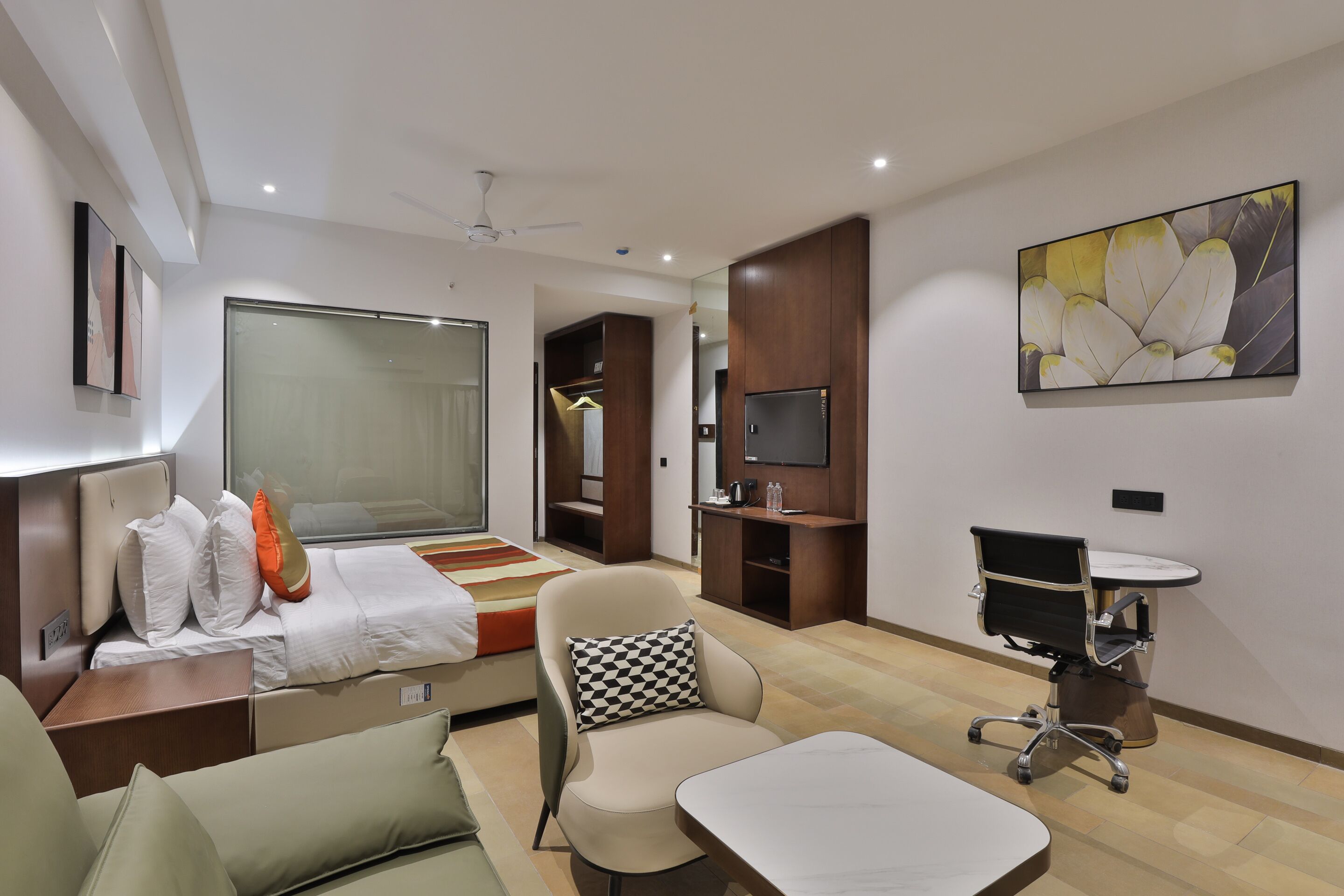 A modern hotel room with a bed, a sofa, a desk, a chair, a TV, and a painting on the wall.
