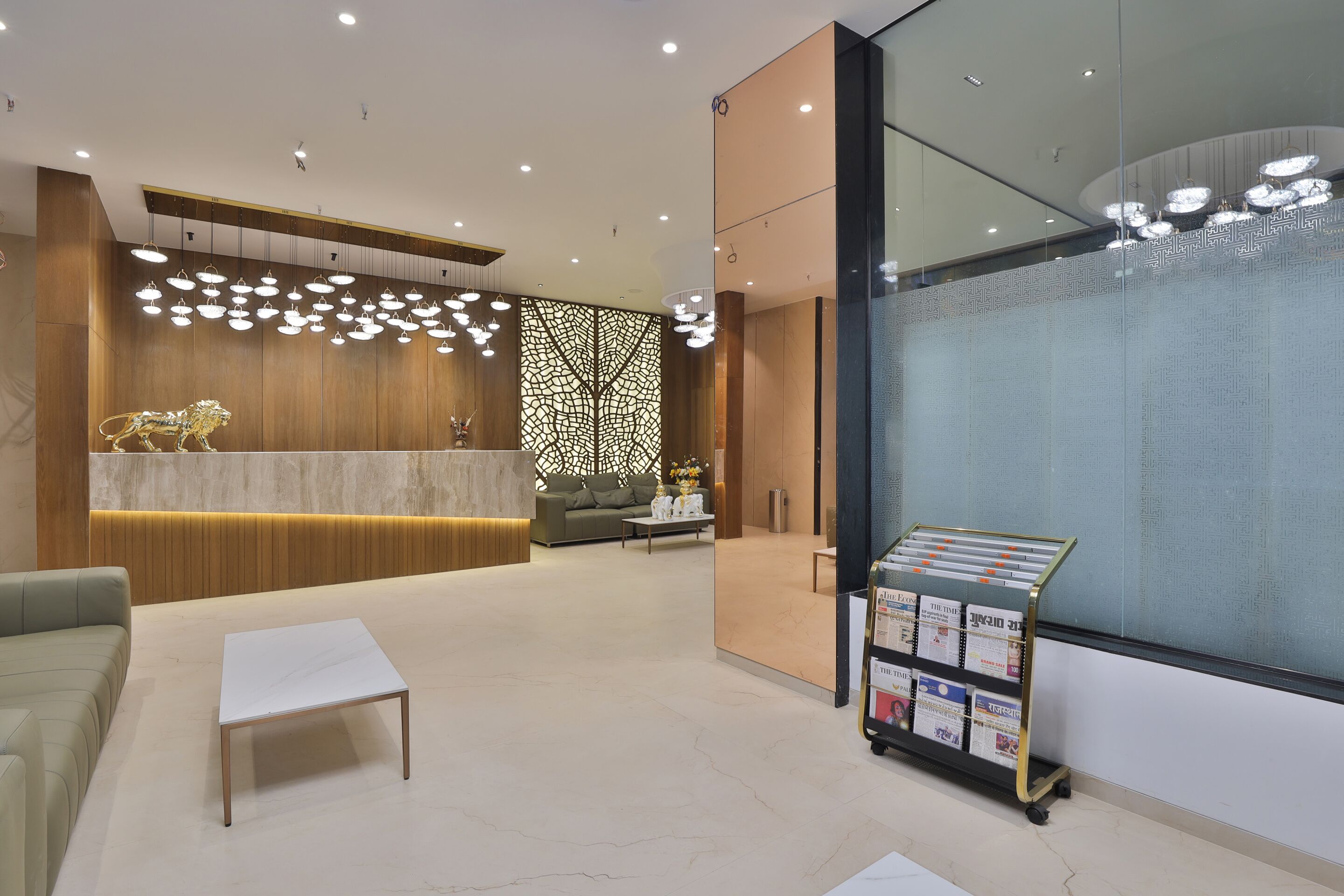 Una zona de recepción moderna con un mostrador de madera, un área de descanso con un sofá y una mesa de centro, y un muro de cristal con un panel decorativo.