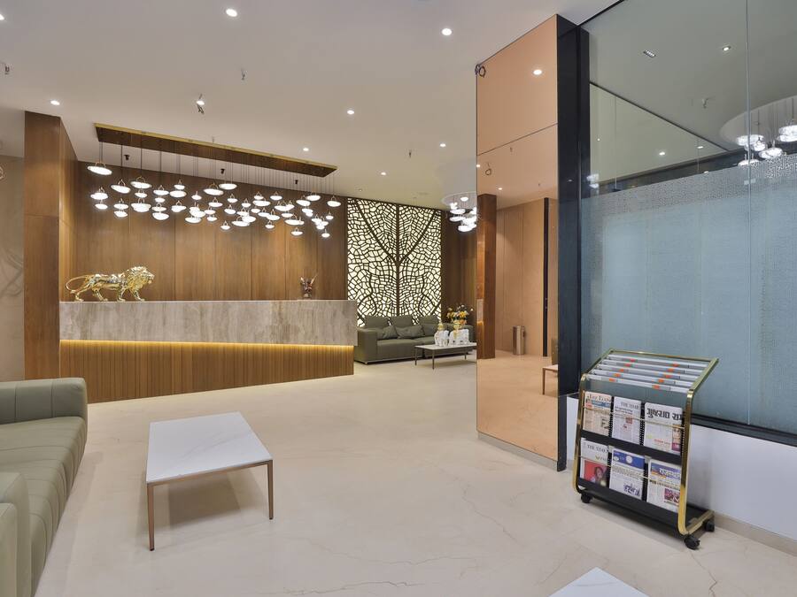 Una zona de recepción moderna con un mostrador de madera, un área de descanso con un sofá y una mesa de centro, y un muro de cristal con un panel decorativo.