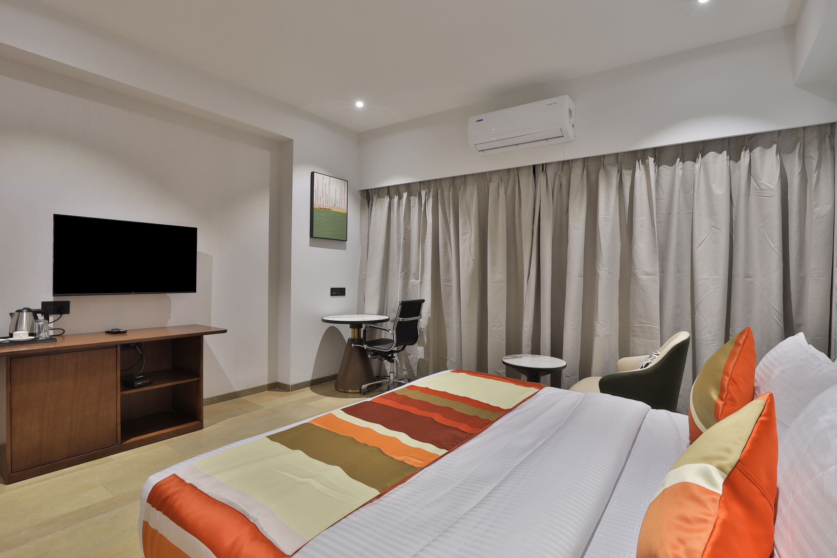 A hotel room with a bed, a desk, a chair, a television, and an air conditioning unit.