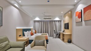 Quarto de hotel moderno com uma cama, um sofá, uma escrivaninha, uma cadeira, uma televisão e obras de arte nas paredes.