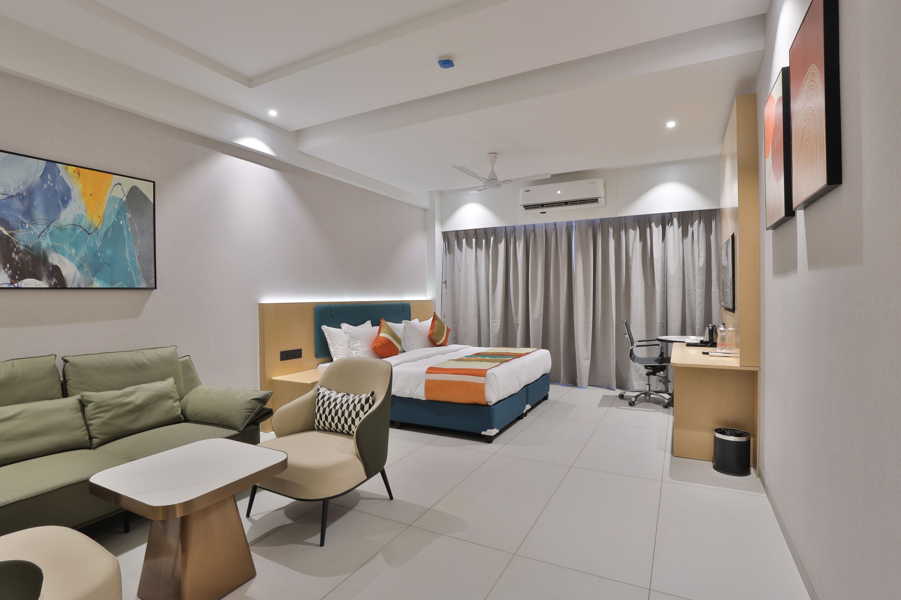 A modern hotel room with a sofa, a chair, a desk, a bed, and a ceiling fan.