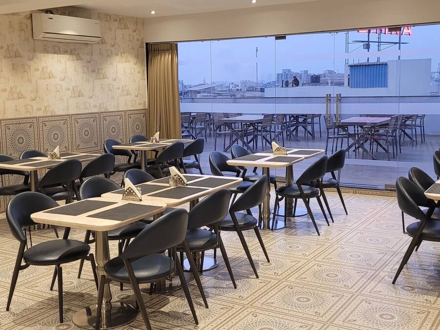 Zona pranzo con tavoli e sedie, pavimento in piastrelle decorate e vista sulla città attraverso ampie finestre.