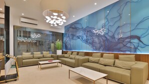 Um hall de hotel moderno com um grande mural abstrato, um sofá de canto, uma mesa de centro e um carrinho.