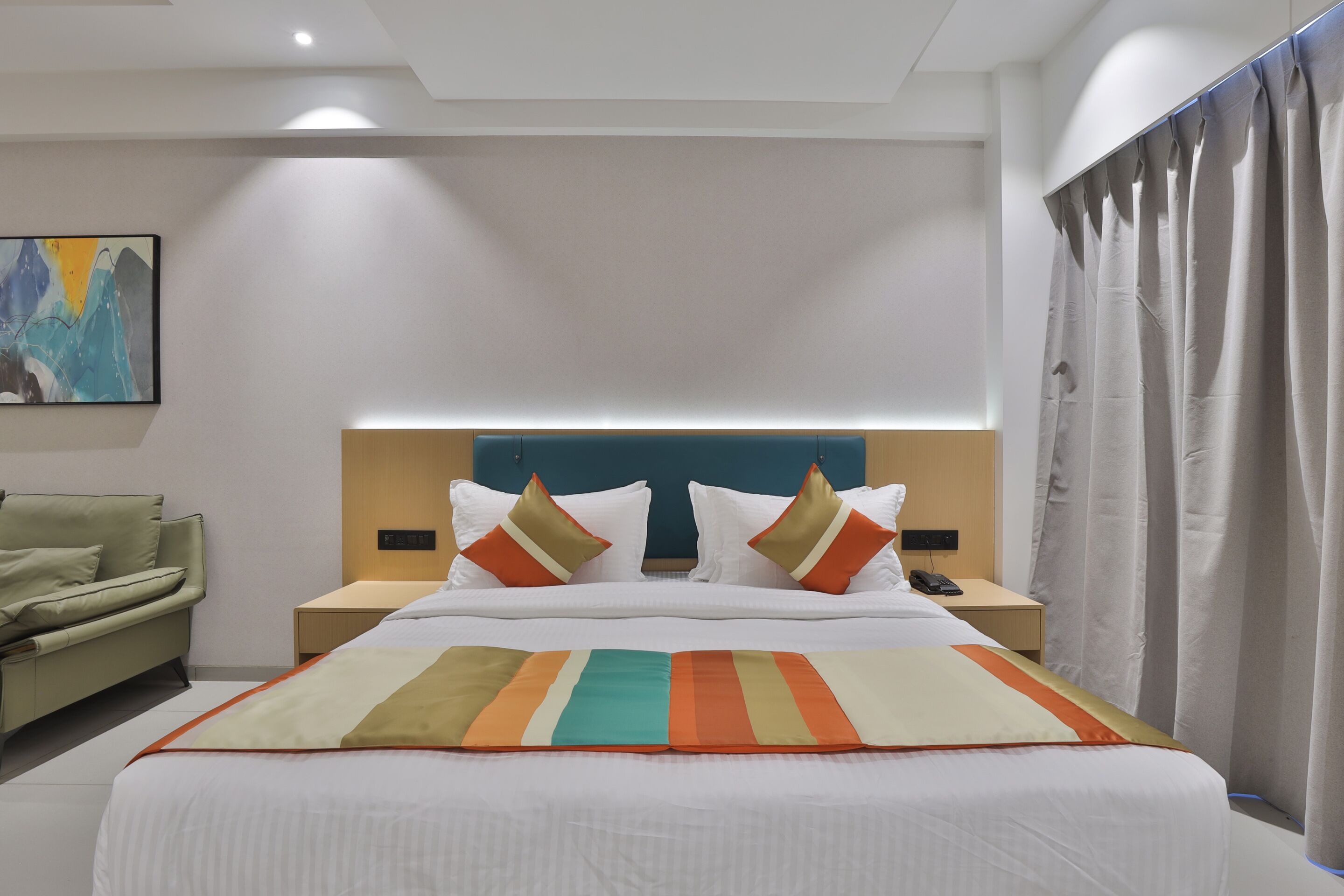 A hotel room with a large bed, a nightstand with a phone, a lamp, and a painting on the wall.