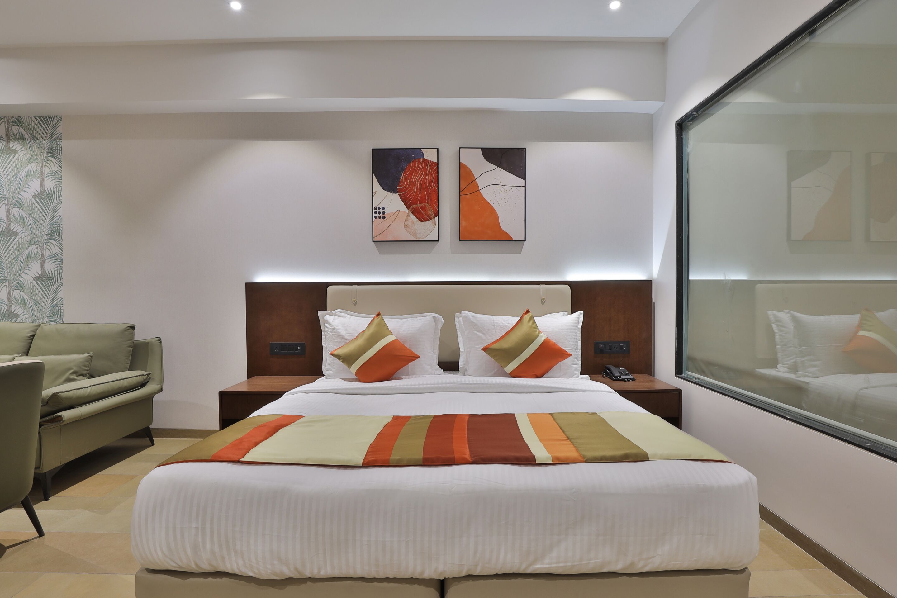 A modern hotel room with a large bed, a sofa, a nightstand, and two abstract paintings on the wall.