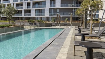 A modern hotel with a swimming pool, outdoor seating, and a multi-story building with balconies.