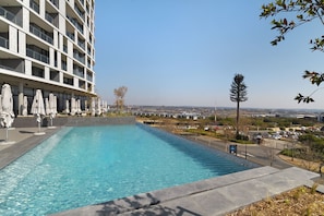 Une piscine entourée de chaises longues et de parasols, le tout adossé à un bâtiment moderne doté de balcons.