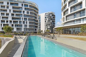 Un immeuble résidentiel moderne doté d’une piscine, de balcons et d’une pelouse bien entretenue.