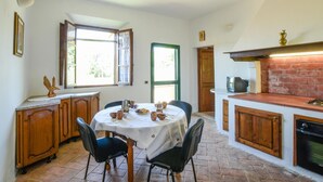 Une cuisine avec une table ronde, des chaises, un four en briques et une fenêtre avec des rideaux.