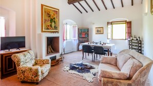 Un salon avec une cheminée, des fauteuils à motifs floraux, un canapé, une table à manger avec des chaises et un meuble à vin.