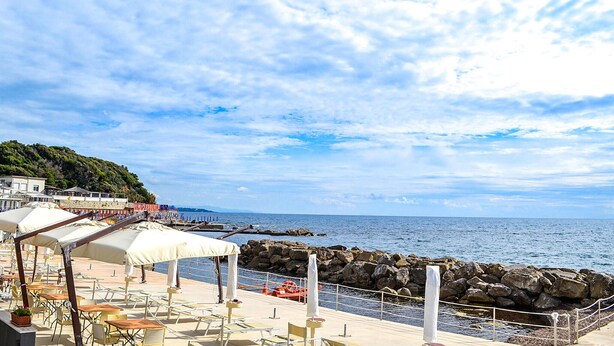 Une terrasse en bord de mer avec des places assises à l’extérieur, un rivage rocheux et une vue sur la mer.