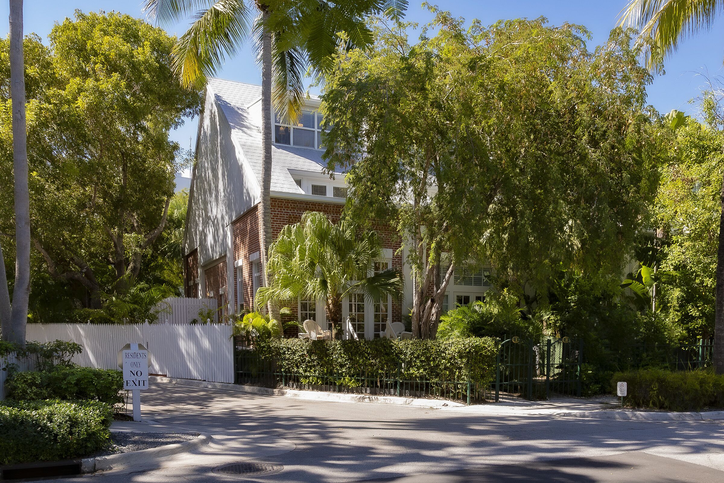 A gated residential area with a white fence, a sign indicating 'RESIDENTS ONLY NO EXIT', and a clear sky.
