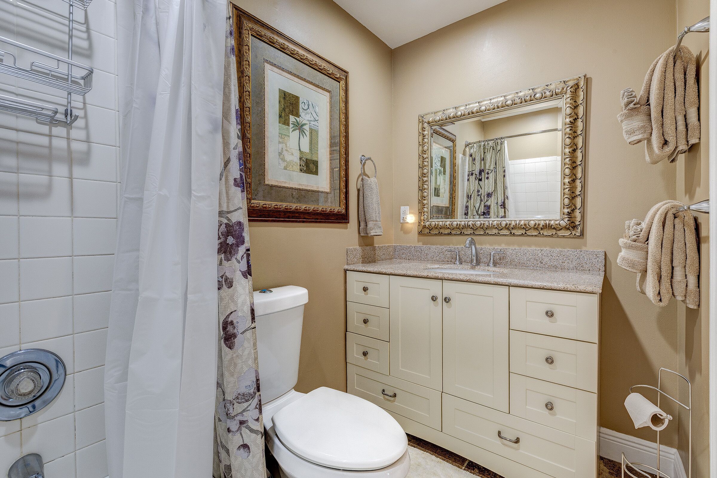 A bathroom with a toilet, sink, vanity, and a shower curtain.
