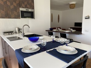 Una cocina moderna con horno empotrado, lavamanos y comedor preparado para seis personas, con manteles individuales azules y platos blancos.