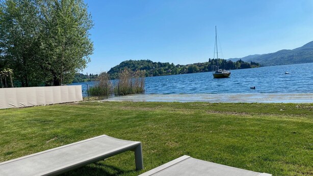 Une vue sur le lac, avec une zone herbeuse, un voilier et, au loin, une rive bordée d’arbres et de collines.