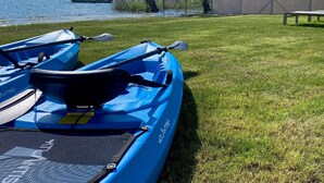 Deux kayaks bleus avec des pagaies, un bateau à toit fermé et une zone herbeuse avec un banc près d’un lac.