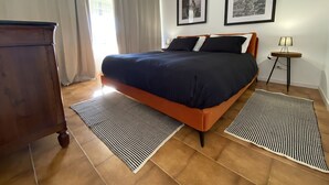 Une chambre à coucher avec un lit, deux tableaux encadrés au mur, une table de chevet avec une lampe et une commode en bois.