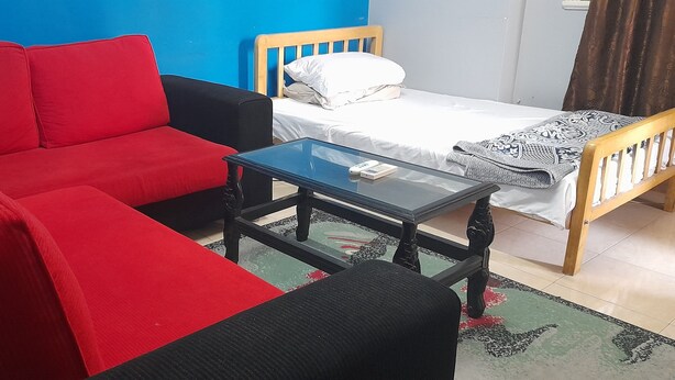 Une pièce avec un canapé rouge, une petite table, un lit avec un oreiller blanc et une couverture à motifs.
