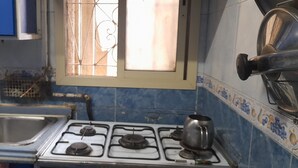 Une cuisine équipée d’une cuisinière à gaz, d’un évier et d’une fenêtre ornée d’une grille décorative.