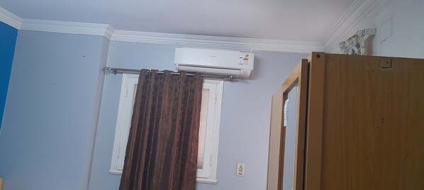 A room with light blue walls, a window with white trim, a brown curtain, and a wooden door.