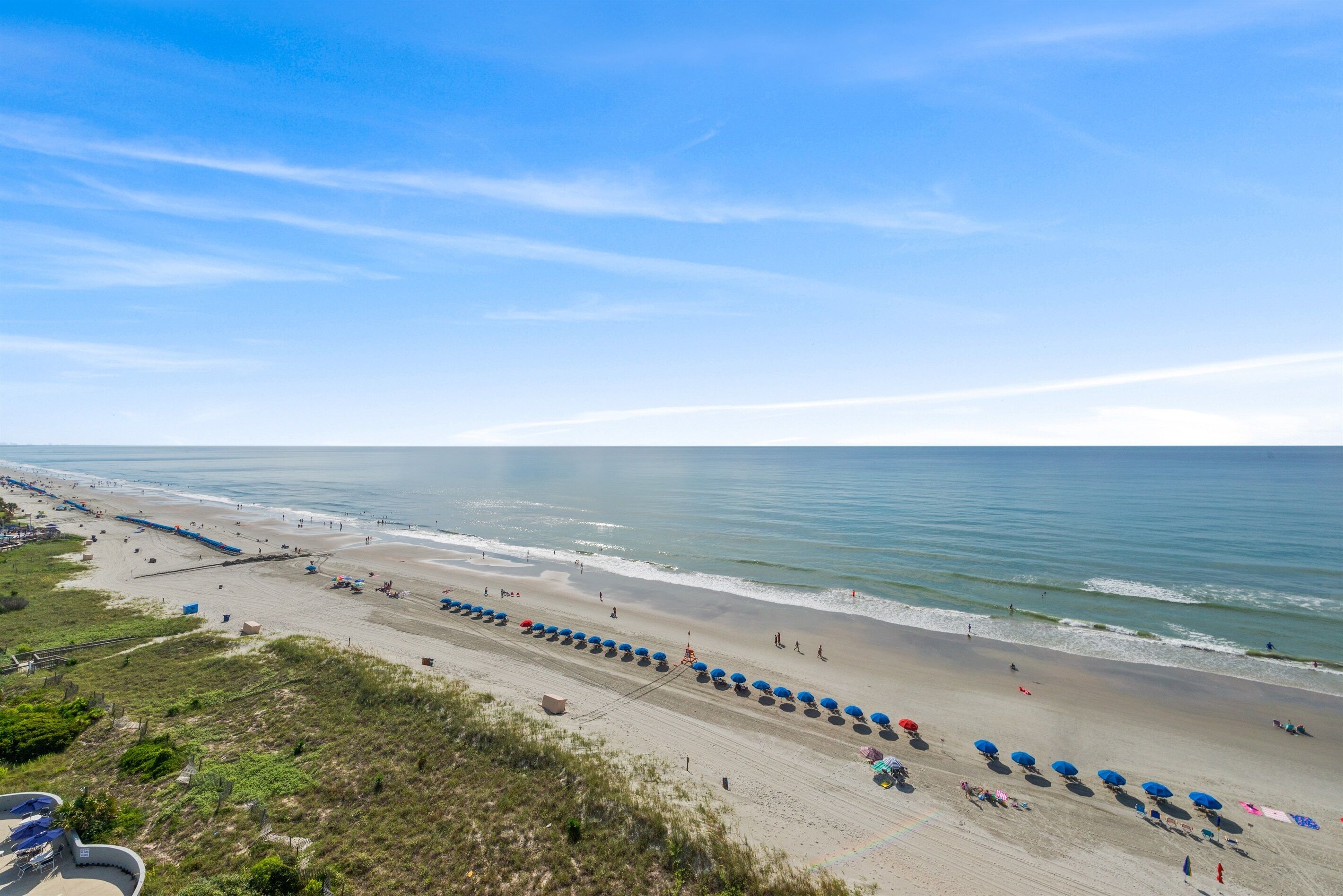 A beach with rows of umbrellas and beach chairs, a sandy shore, and the ocean.