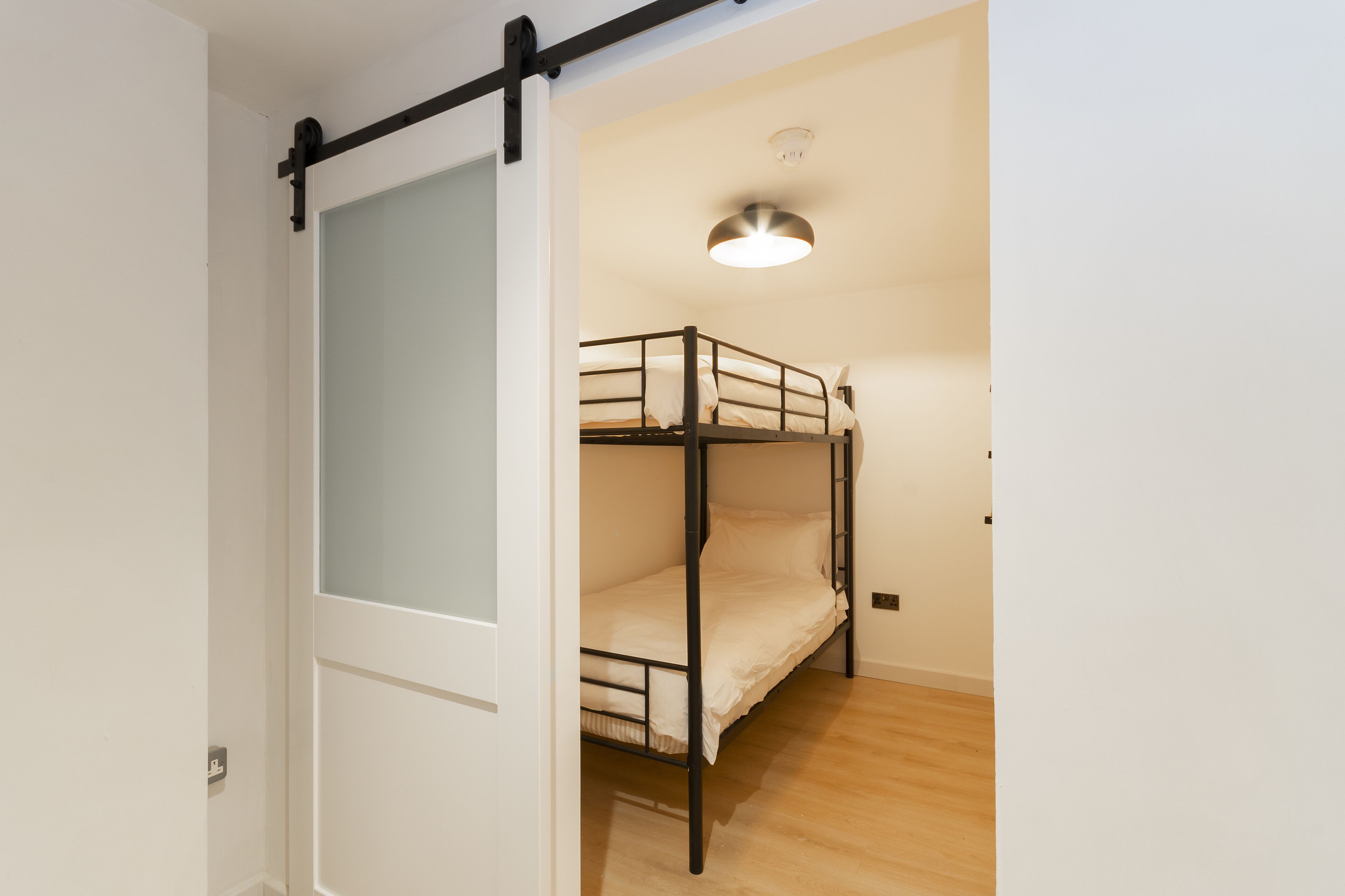 Quarto com beliche, porta deslizante e luminária no teto.