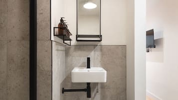 A bathroom with a white sink, a mirror, and a soap dispenser on a shelf.
