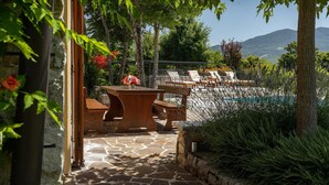 Eine Terrasse im Freien mit Steinböden, Holzmöbeln und Blick auf einen Pool und Berge.