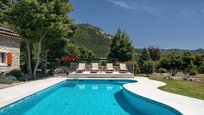 Ein Pool mit geschwungener Kante, umgeben von einem Steinhaus und üppiger Bepflanzung.