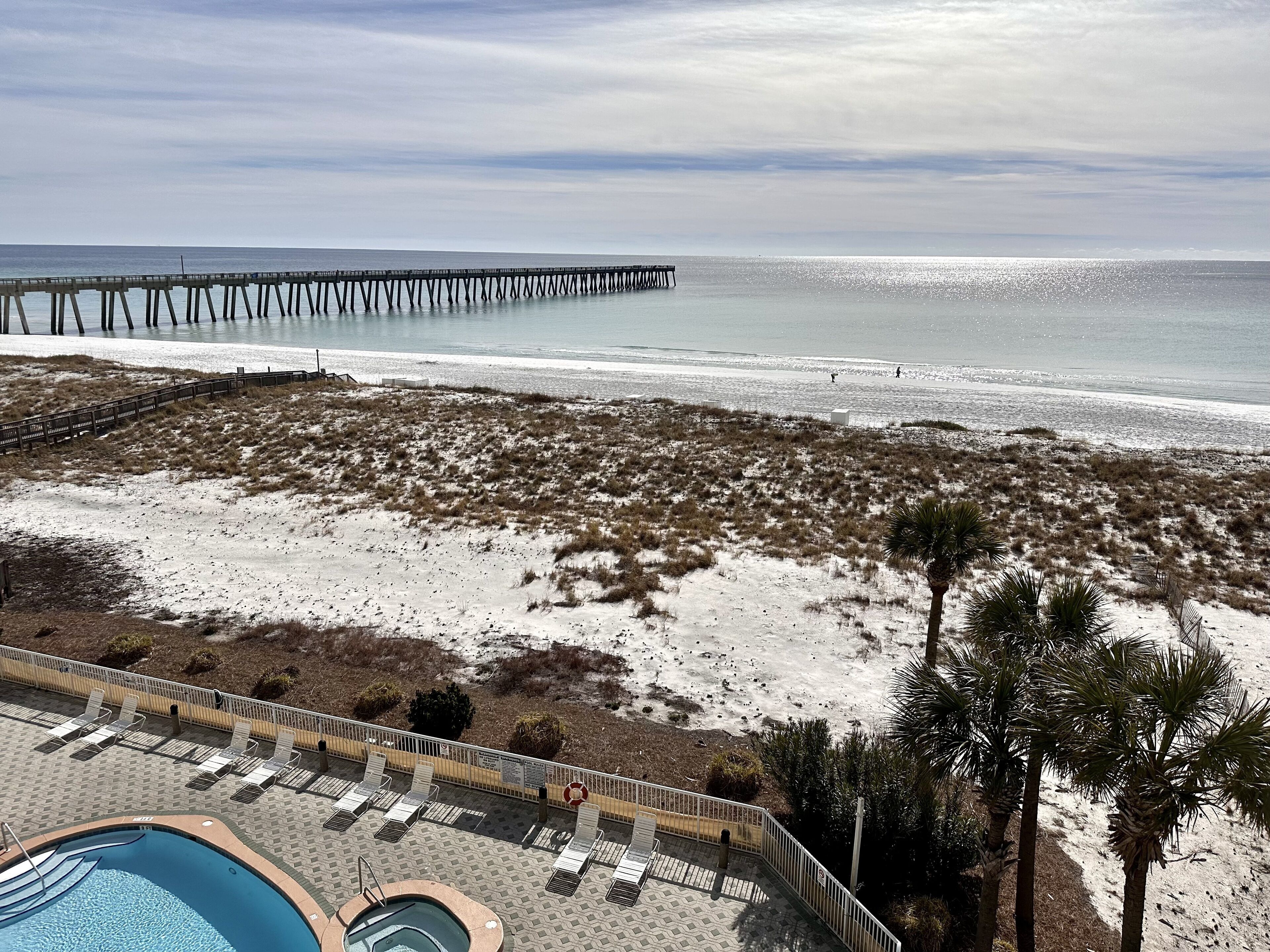 A beach view with a pier extending into the ocean, a swimming pool, and lounge chairs.