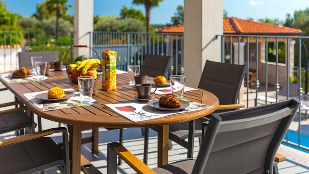 An outdoor dining area with a table set for two, featuring a basket of fruits, a juice carton, and a croissant. - Stunning home in Porec (Porec)