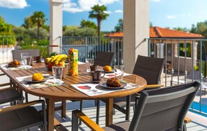 An outdoor dining area with a table set for two, featuring a basket of fruits, a juice carton, and a croissant. - Stunning home in Porec (Porec)