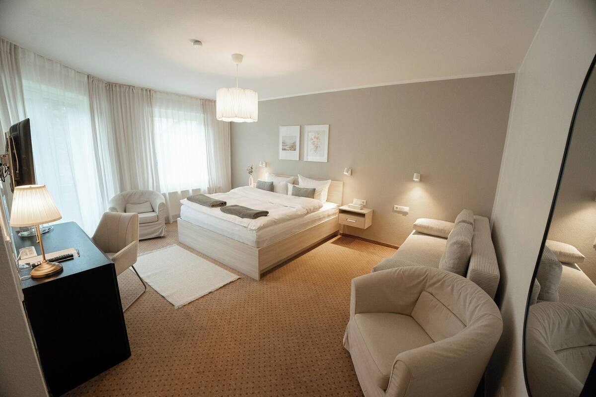 Ein modernes Hotelzimmer mit einem großen Bett, einem Schreibtisch mit Lampe, einer Couch und einem Spiegel.